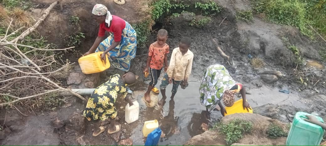 Community members collecting water from a shallow stream